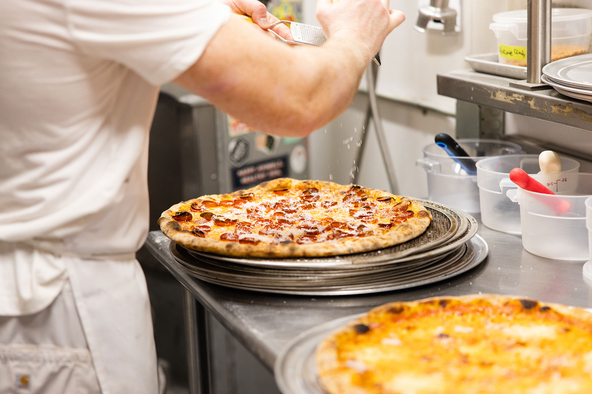 a pizza chef sprinkles parmesan cheese on a freshly-made pepperoni pizza in the pizza thief kitchen