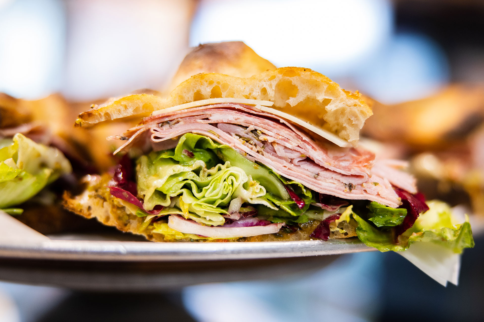 a pizza thief focaccia sandwich with deli meats and greens on a plate held by a server